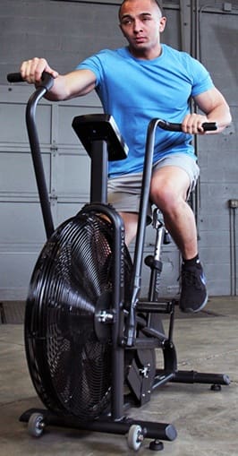 Person riding a stationary exercise bike indoors wearing casual clothing.
